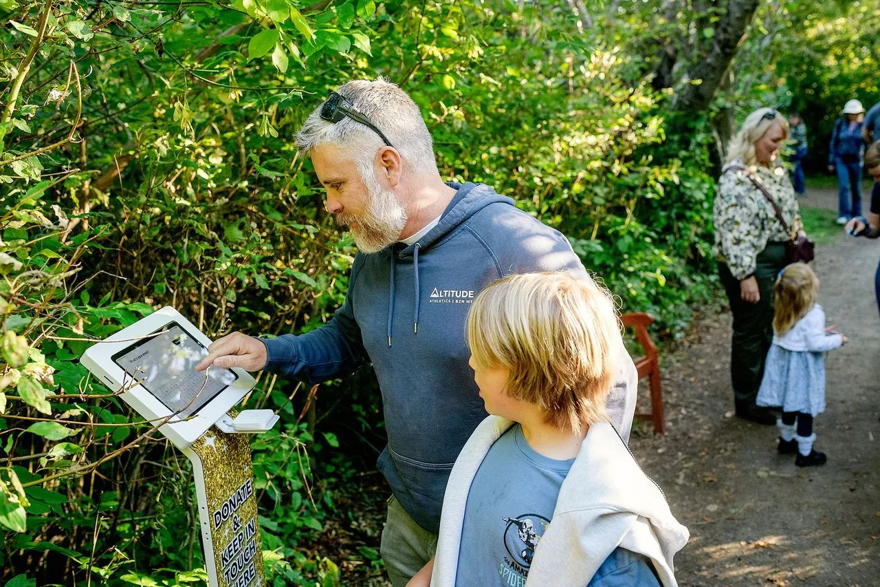 A visitor and his son giving at a Full Size kiosk with a custom banner on a nature trail